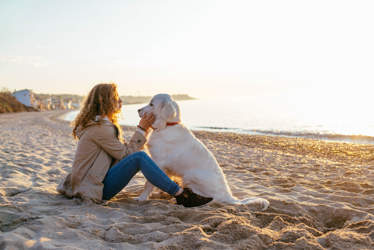 Sjöbogårdens bild på kvinna med hund på strand i solnedgång. 