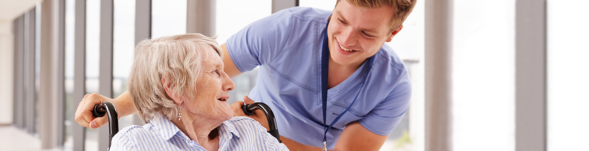 13114212-nurse-pushing-senior-patient-in-wheelchair-along-corridor.jpg