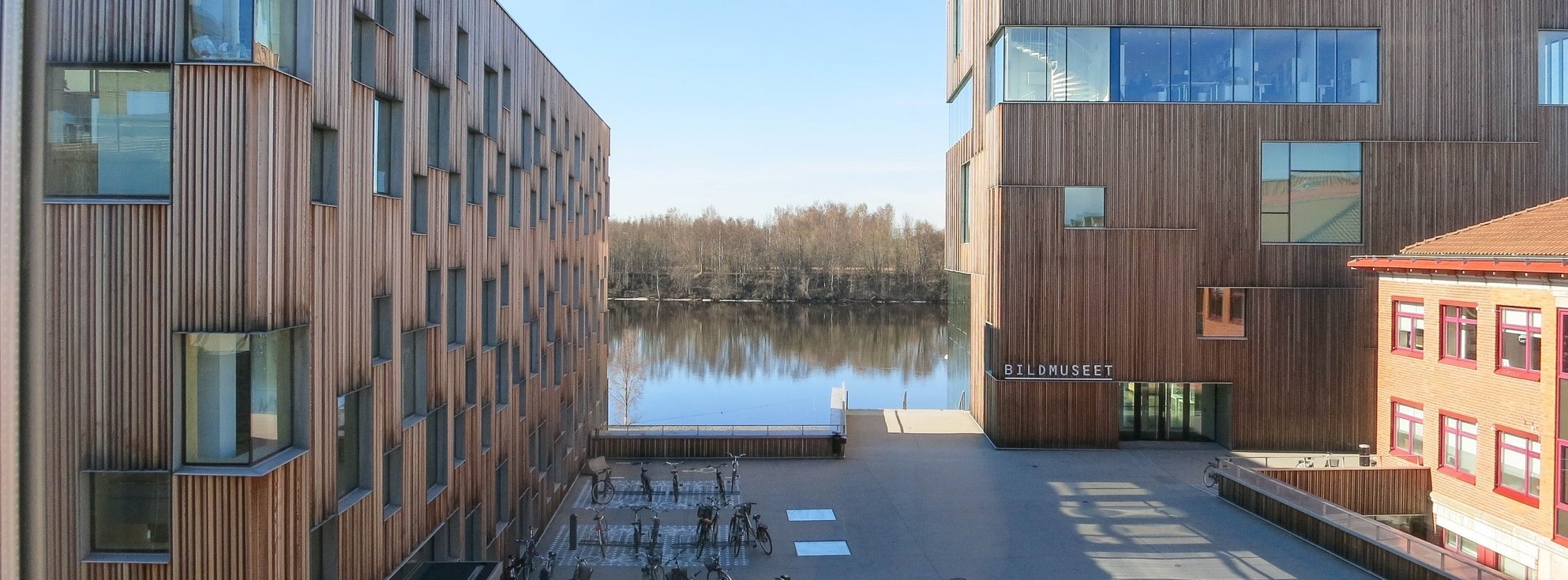 Bilden visar Konstnärligt campus som är byggd av trä och visar upp enspännande arkitektur . Bakom husen syns Umeåälv.