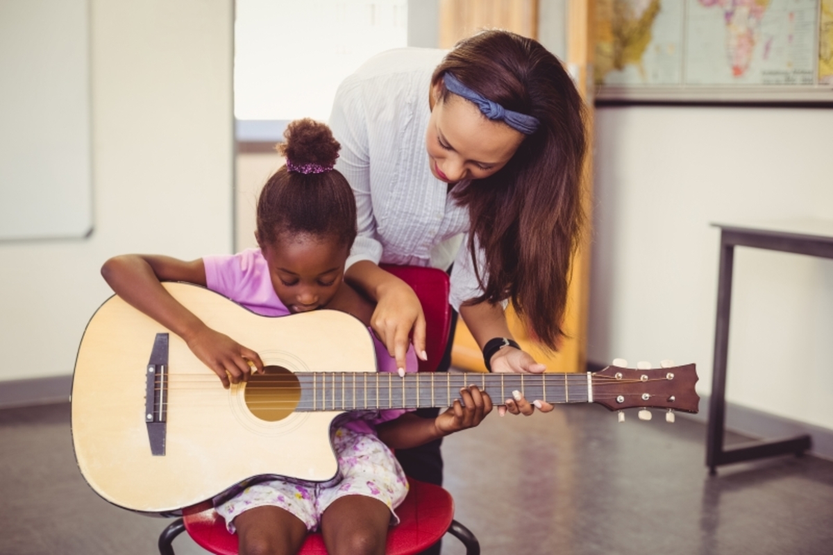16152973-teacher-assisting-a-girl-to-play-a-guitar-in-classroom.jpg