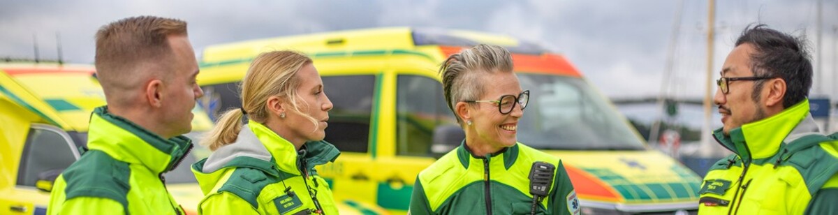 Ambulanspersonal, två män och två kvinnor, står framför ambulanser och pratar med varandra.jpg