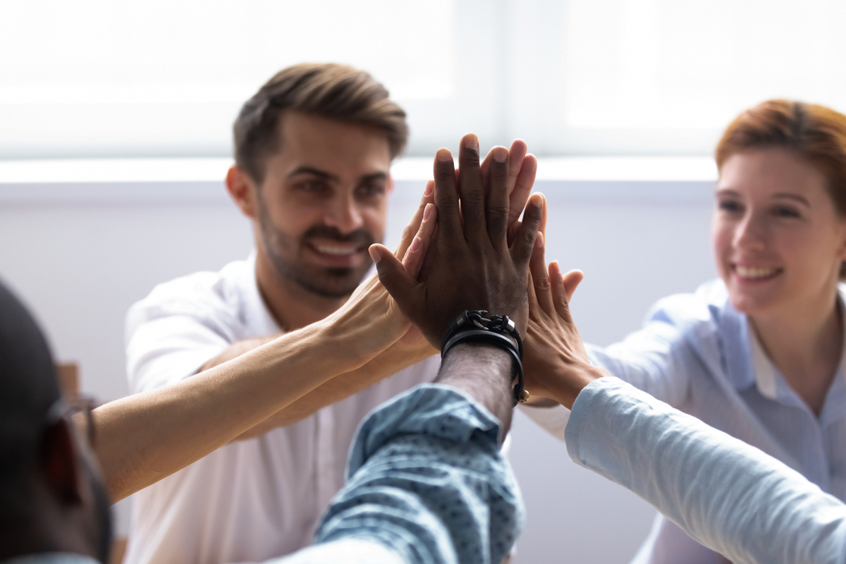 Fem personer gör high five med varandra på arbetsplats