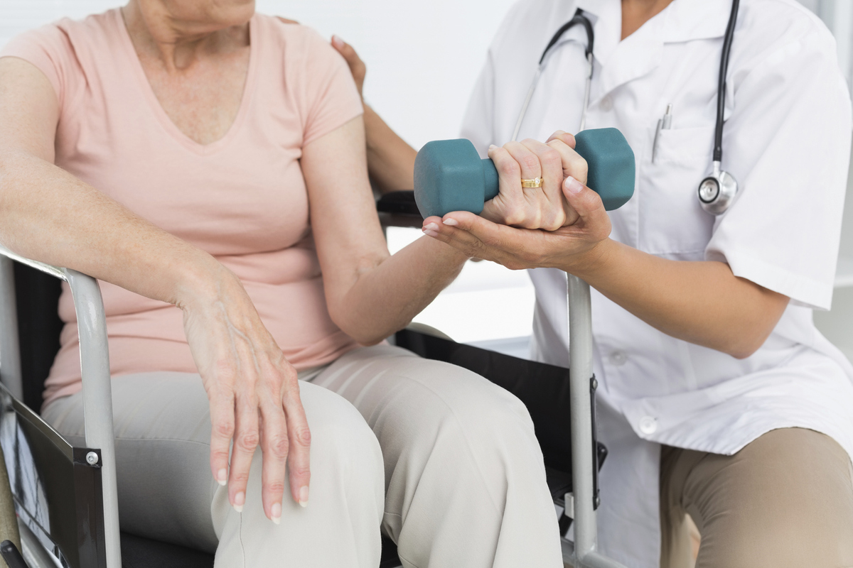Fysioterapeut hjälper äldre kvinna att träna med hantlar.