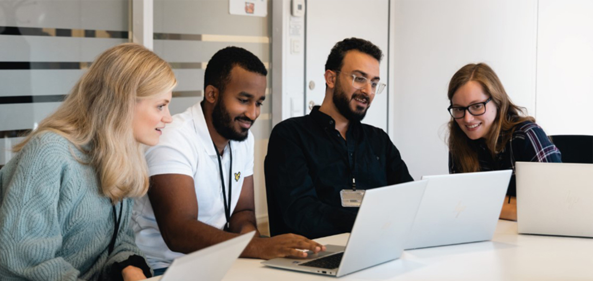 Två kvinnor och två män sitter och samarbetar vid laptops. IT-trainee 2024.jpg