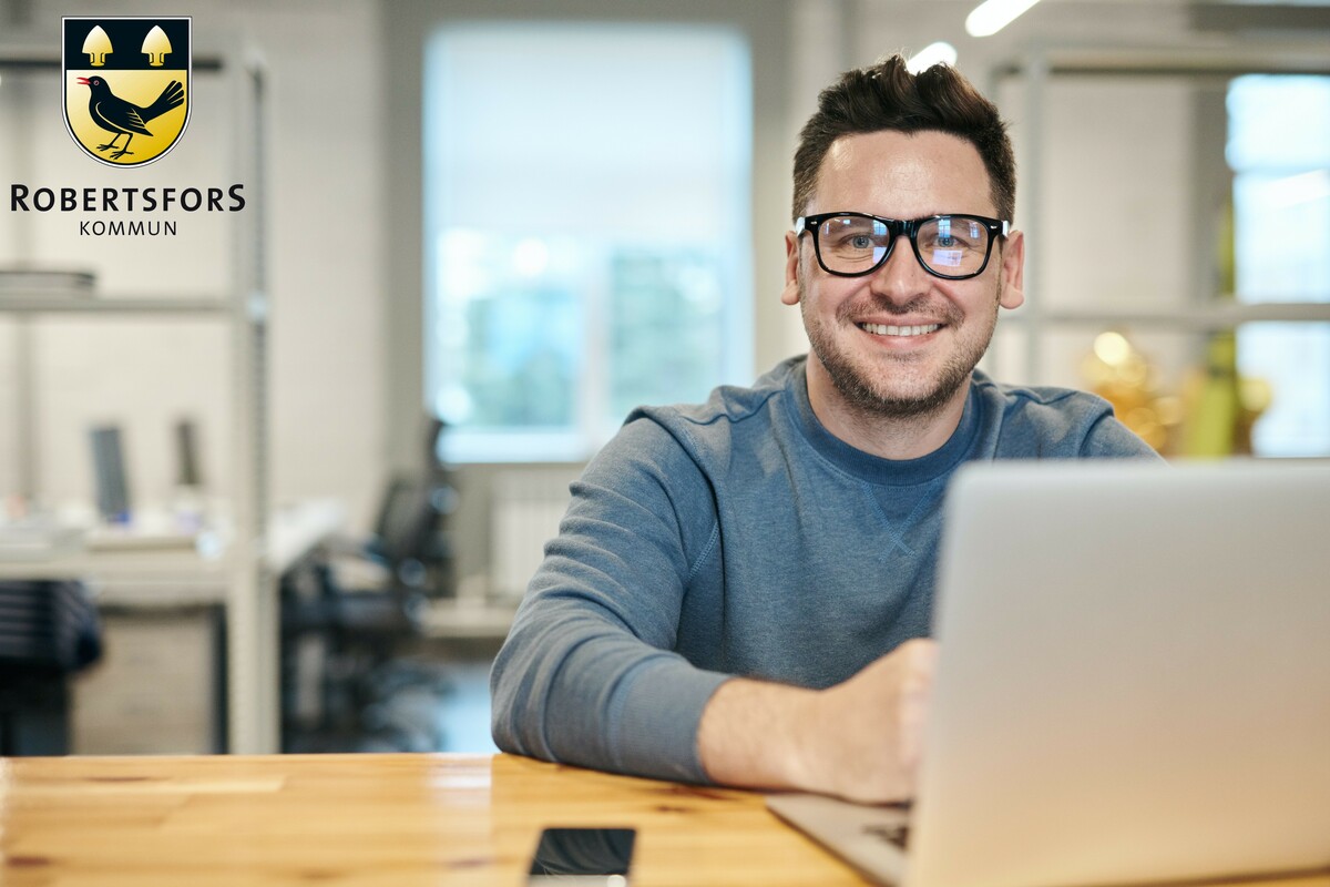 En leende man med glasögon som sitter vid en dator