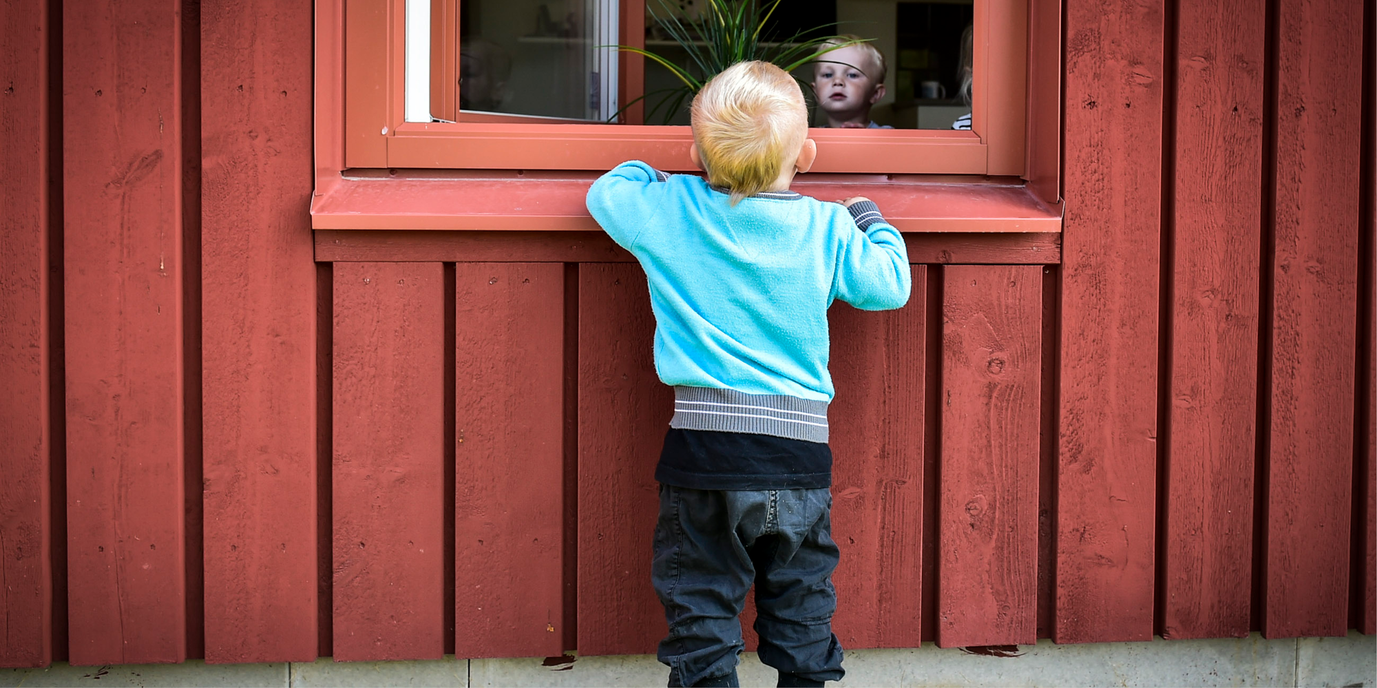 Barn i blå tröja kikar in genom ett fönster där hen ser ett nyfiket barn kika ut. 