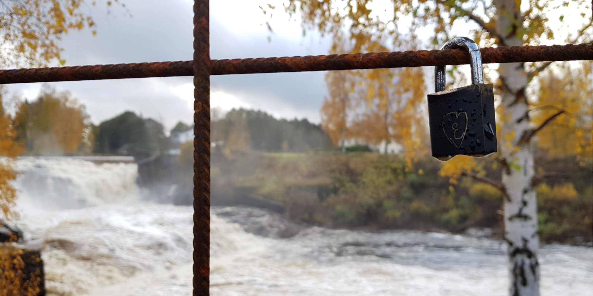 Hänglås som sitter på ett rostigt armeringsjärn. I bakgrunden syns Munkforsen, Klarälvens högsta vattenfall. 