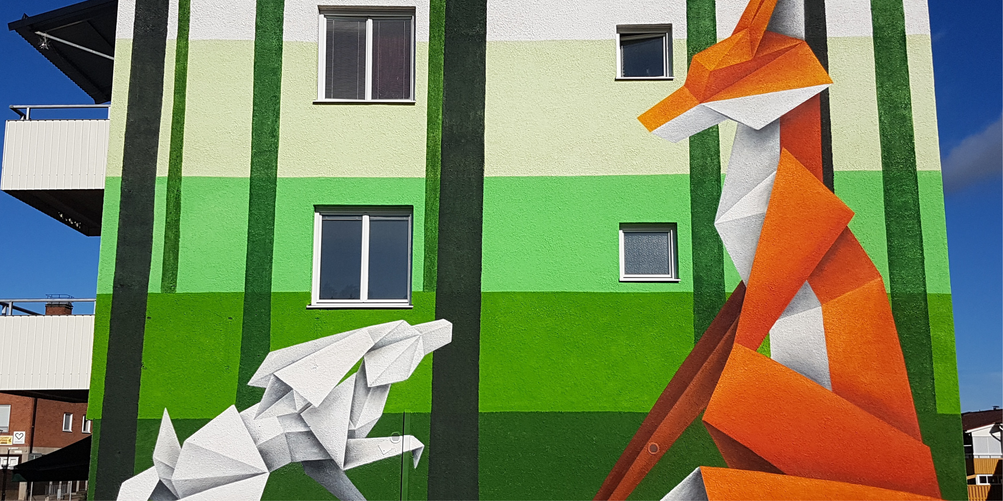 Geometrisk väggmålning i centrala Munkfors som föreställer en orange räv och vit kanin. 