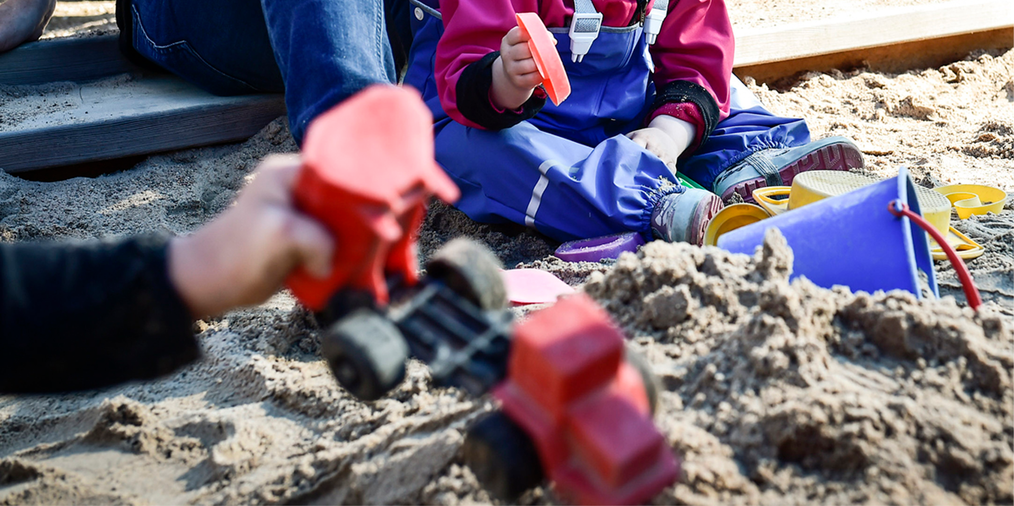 Barnhänder som leker med plastleksaker i en sandlåda. 